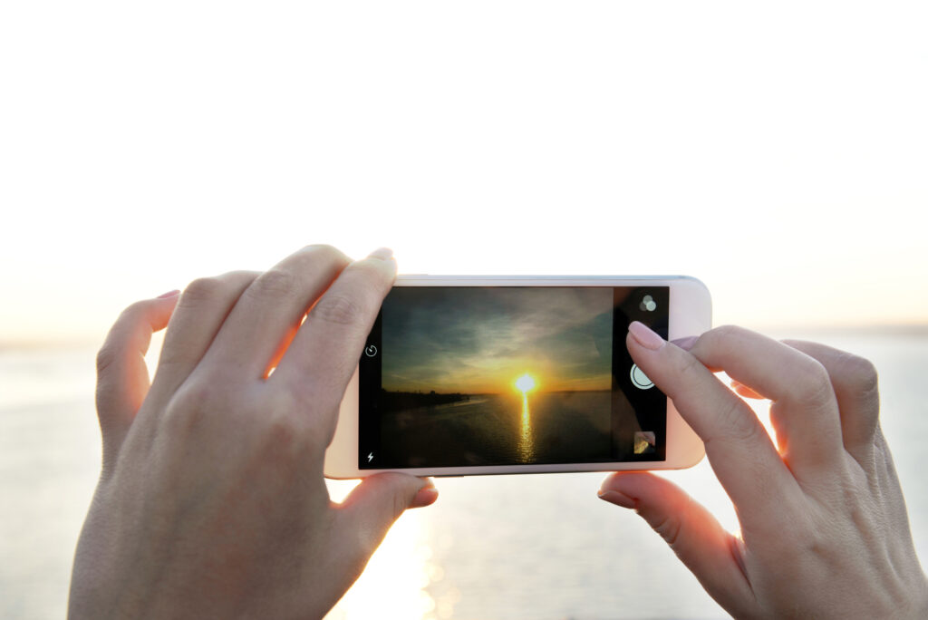 Female hands holding smart phone and taking photo of sunset