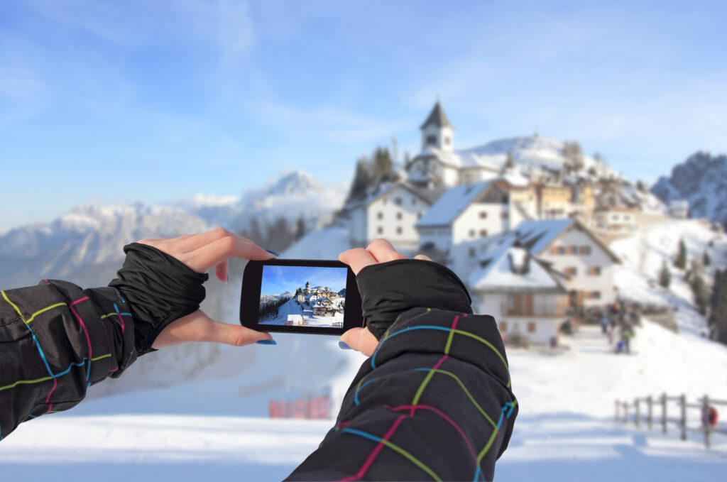 Photographing a cell phone, winter landscape, idyllic village Monte Lussari, Italy