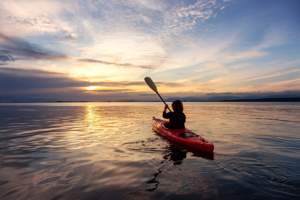 Sea Kayaking in calm waters during a colorful and vibrant sunset. Adventure Girl in Red Kayak.