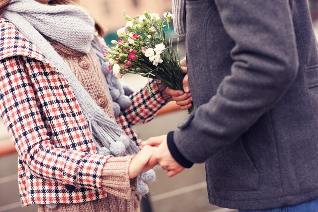 A midsection of a couple holding hands and flowers