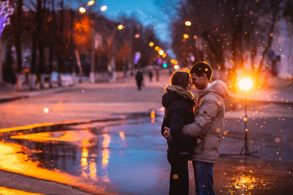 In love couple kissing in the snow at night city street. Filtered with grain and light flashing