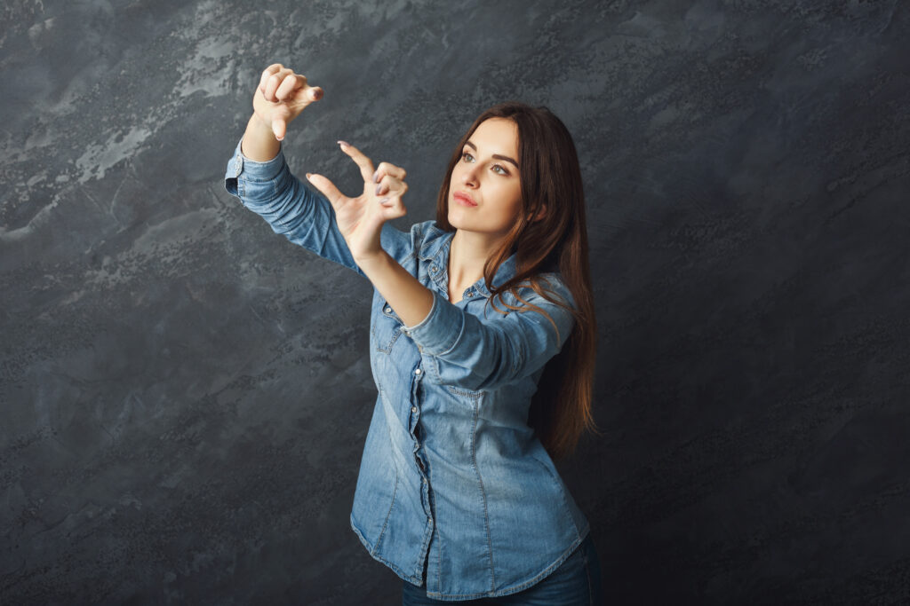 Serious girl holding virtual smartphone or framing a photo shot with fingers at black studio background, copy space