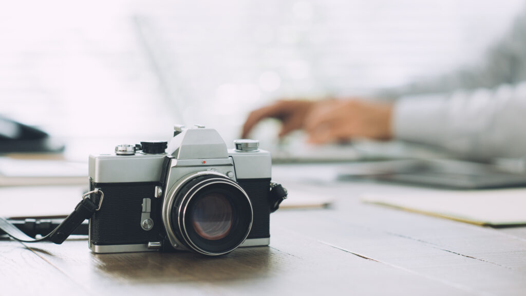 Professional photographer working with a computer at the communication agency and vintage camera on the foreground