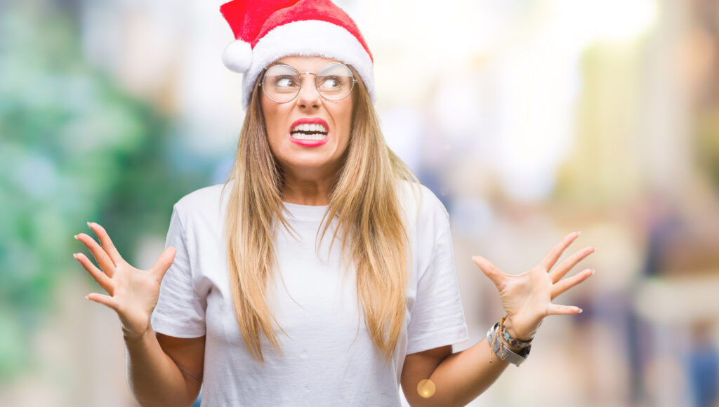 Young beautiful woman wearing christmas hat over isolated background crazy and mad shouting and yelling with aggressive expression and arms raised. Frustration concept.