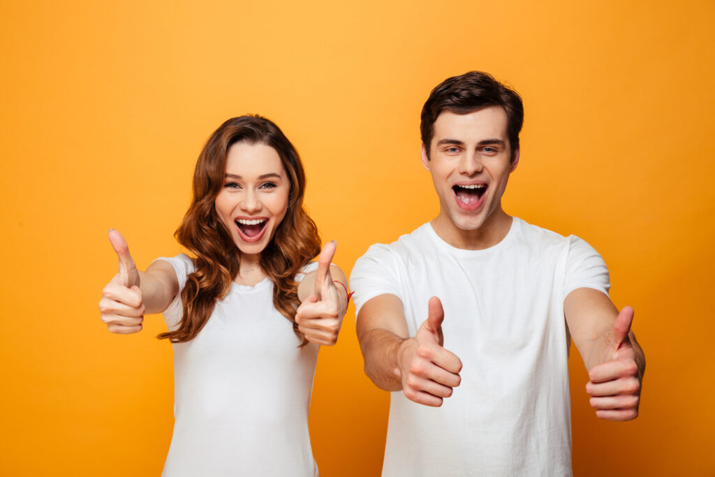 Happy young lovely couple showing thumbs up and looking at the camera over yellow backgroun