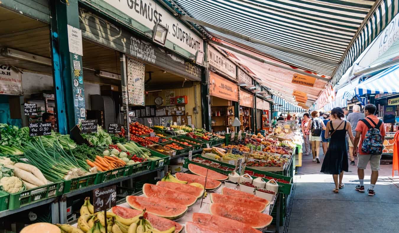 People walking down the aisles of produce at the Naschmarkt, and outdoor market in Vienna, Austria