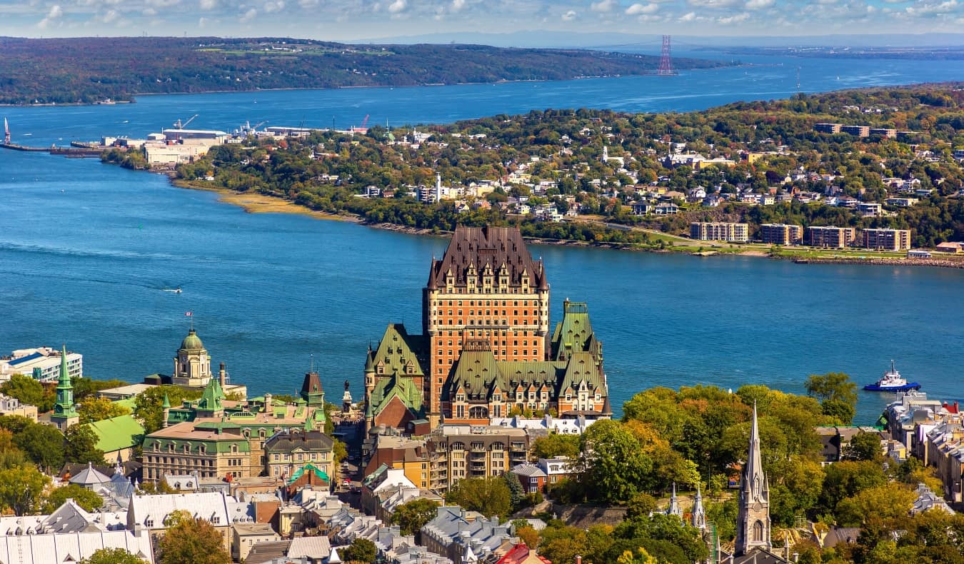 Panoramic aerial view of Quebec City in Canada, with Frontenac Castle as a prominent feature of the skyline and the deep blue of the Lawrence River in the background