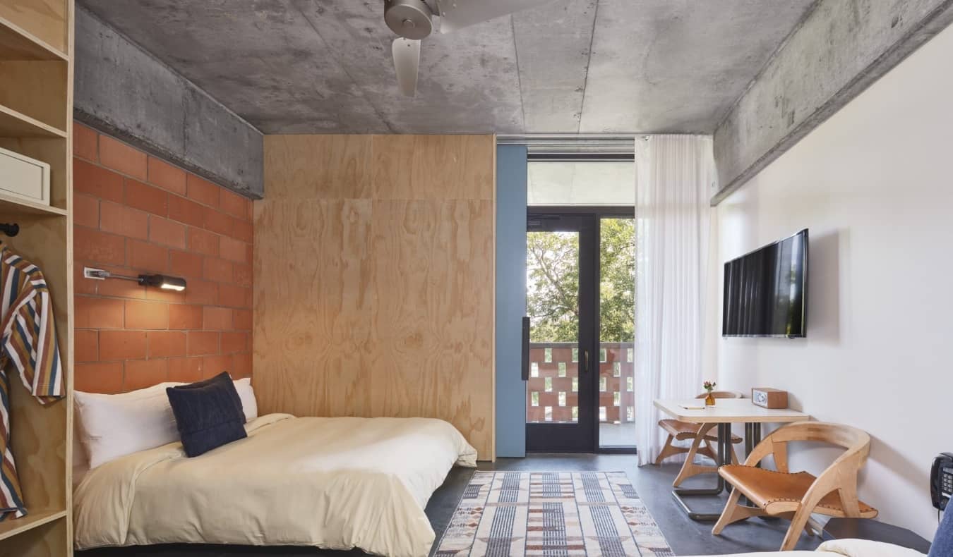 Guest room with an exposed brick wall, terrace, and wooden desk at The Carpenter Hotel in Austin, Texas