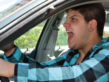 An irritated young man driving a vehicle is expressing his road rage.