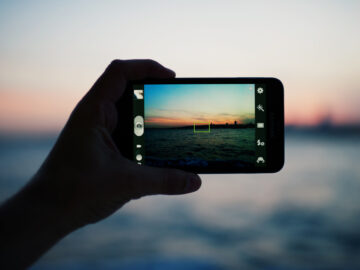 Person taking a photo of amazing sunset using smart phone camera, tourist hand holding cell phone while taking a photograph of nature landscape in travel,taking a picture of outdoors, blur background