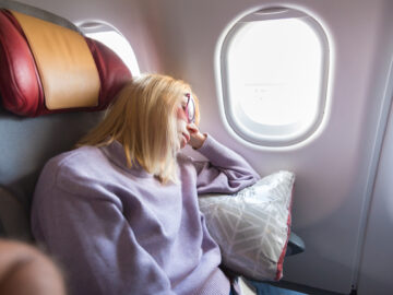 Tired blonde casual caucasian woman sleeping on seat while traveling by airplane on long distance transatlantic flight. Commercial transportation by planes.