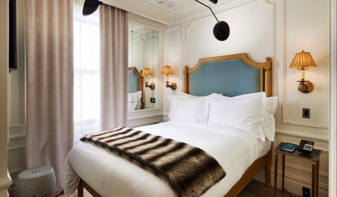 Stately hotel room with a gilded headboard, lamps on either side of the bed, and white crown molding on the walls at The Marlton Hotel in NYC