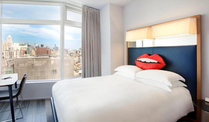 Sunny hotel room with exposed brick walls, a double bed, and a flatscreen TV on the walls at East Village Hotel in NYC