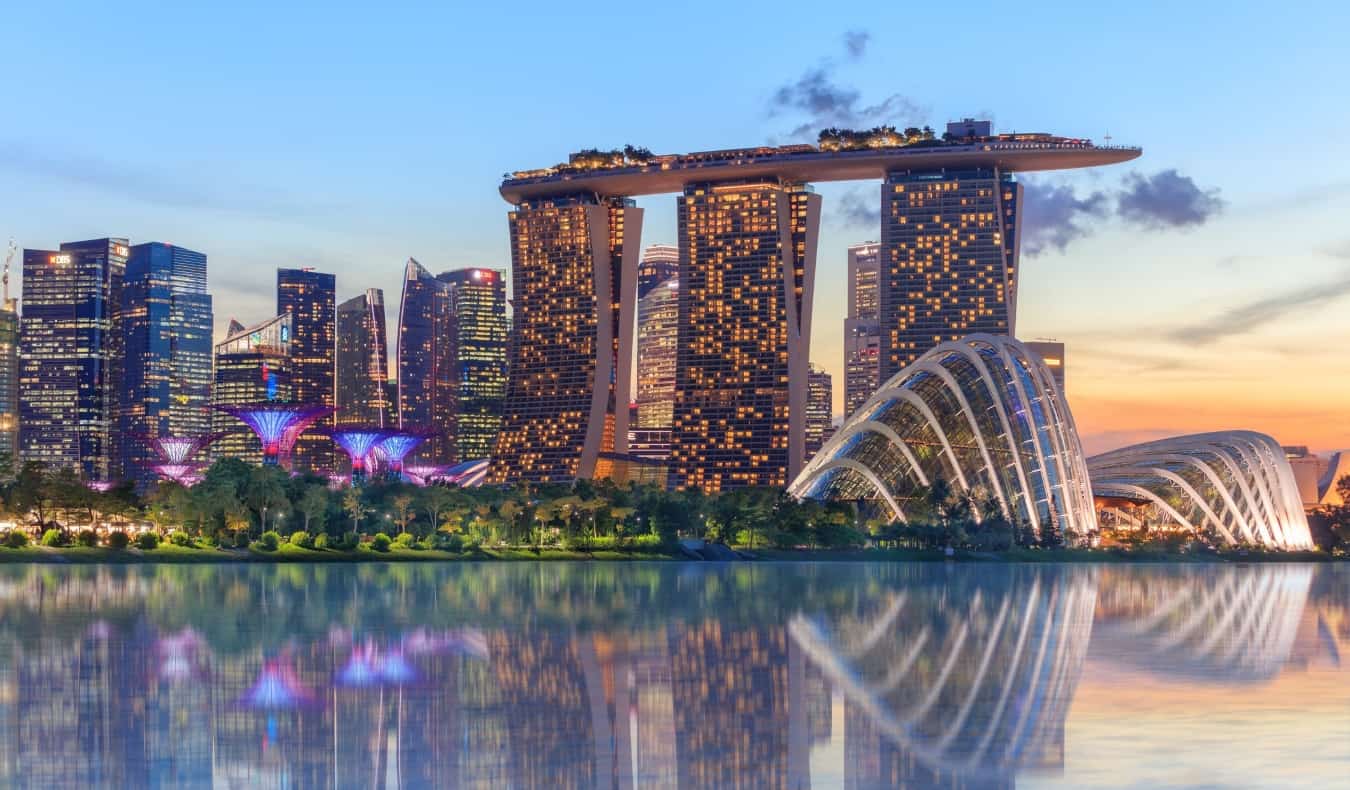 Singapore's supertree grove, cloud garden greenhouse and Marina Bay Sands hotel reflecting in water at dusk with glowing lights